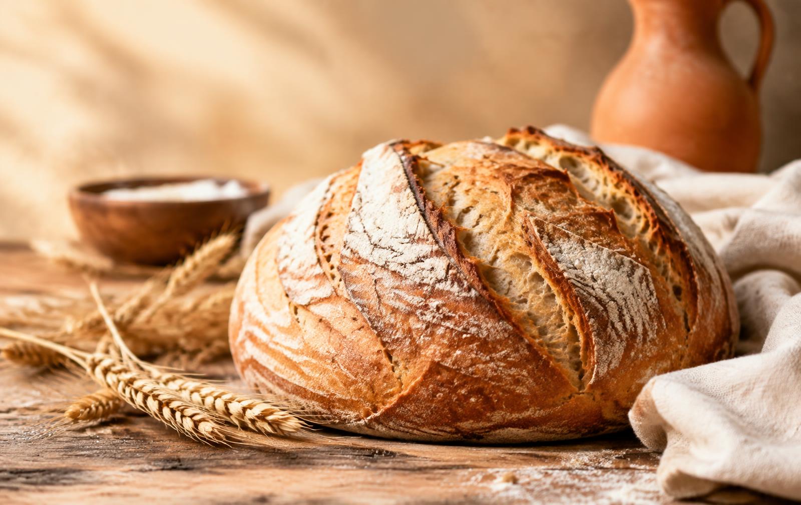 A golden-crusted sourdough boule on a wooden table with wheat stalks
